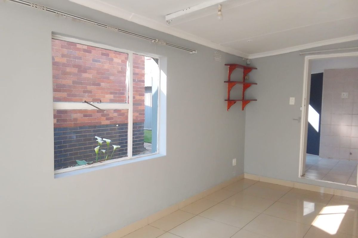 A bright, empty living area featuring neutral tiled flooring, clean grey walls, and a large window providing natural light.