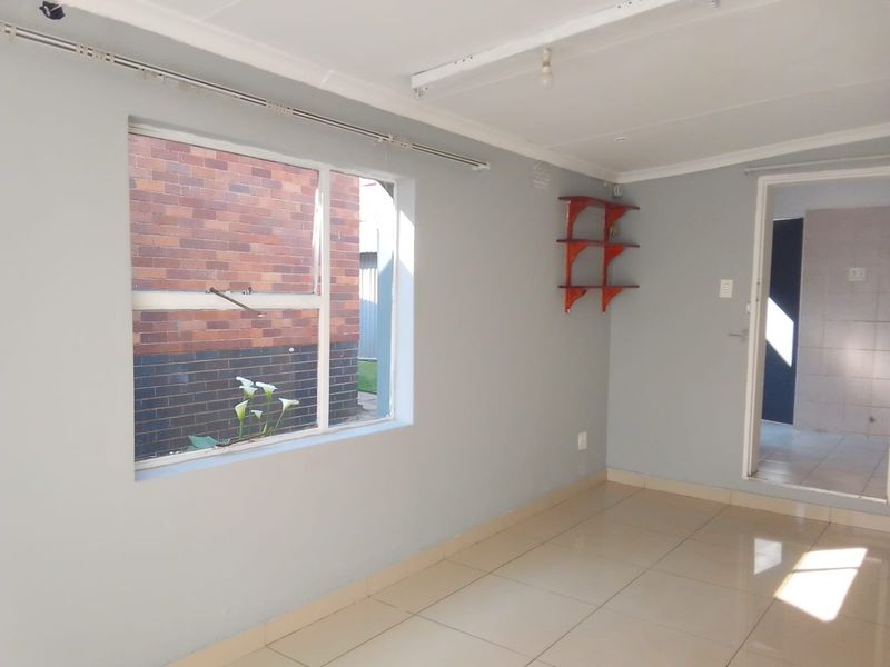 A bright, empty living area featuring neutral tiled flooring, clean grey walls, and a large window providing natural light.