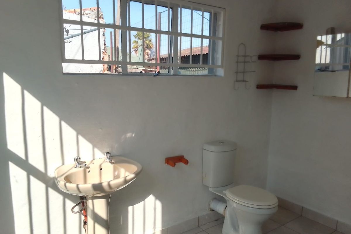 A functional bathroom featuring a pedestal basin, toilet, tiled flooring, and security bars on the window, offering a basic layout ready for updates.