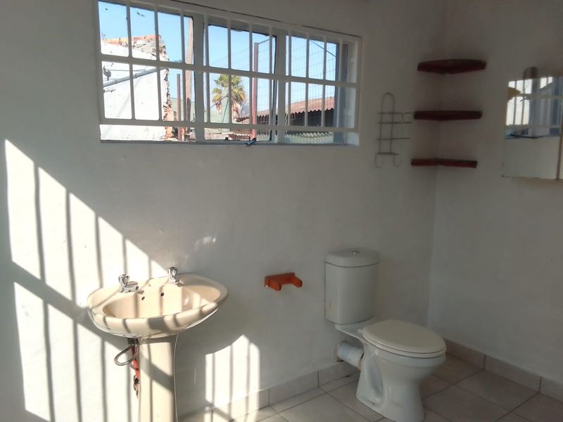 A functional bathroom featuring a pedestal basin, toilet, tiled flooring, and security bars on the window, offering a basic layout ready for updates.