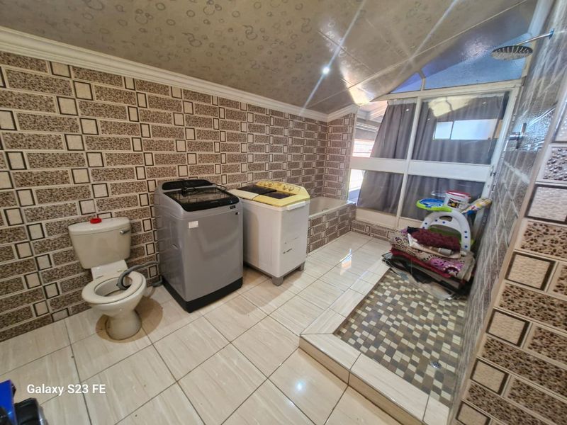A combined bathroom and laundry area featuring tiled walls and flooring, a built-in bathtub, and a shower fixture.