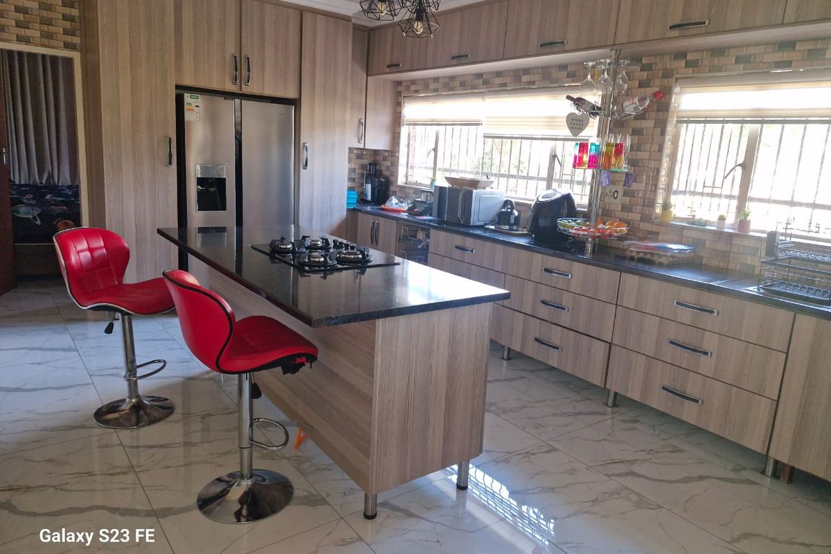 Modern kitchen featuring wood-finish cabinetry, granite countertops, a central island with a gas hob, and polished marble-look floor tiles.