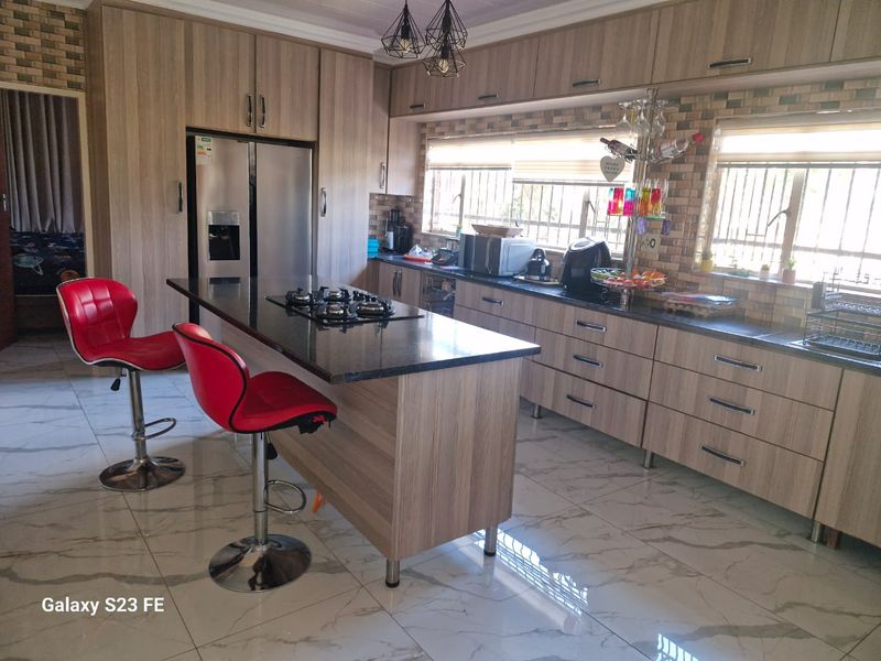 Modern kitchen featuring wood-finish cabinetry, granite countertops, a central island with a gas hob, and polished marble-look floor tiles.