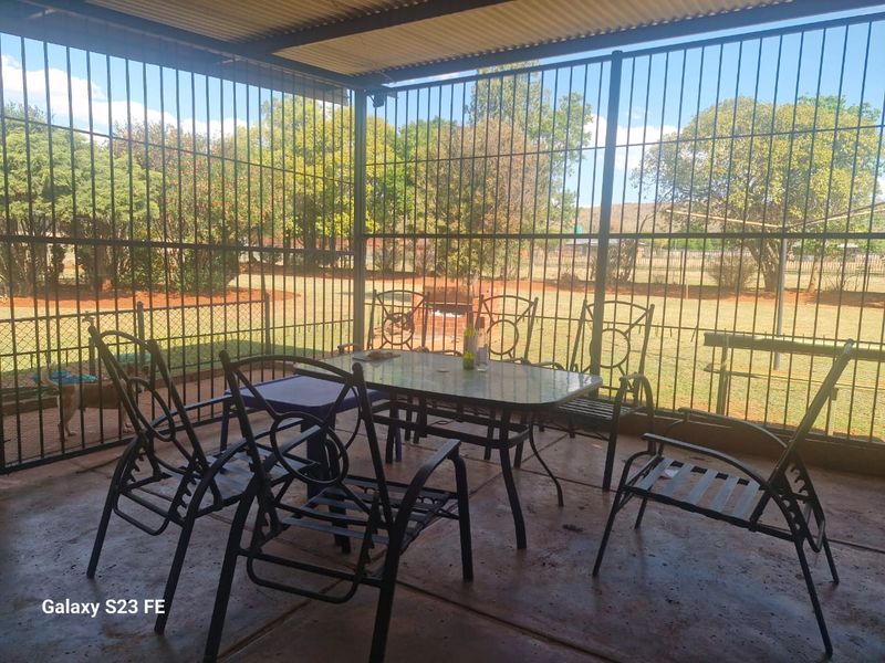 Covered outdoor patio area featuring concrete flooring, security bars, and a built-in braai, overlooking the farm garden.