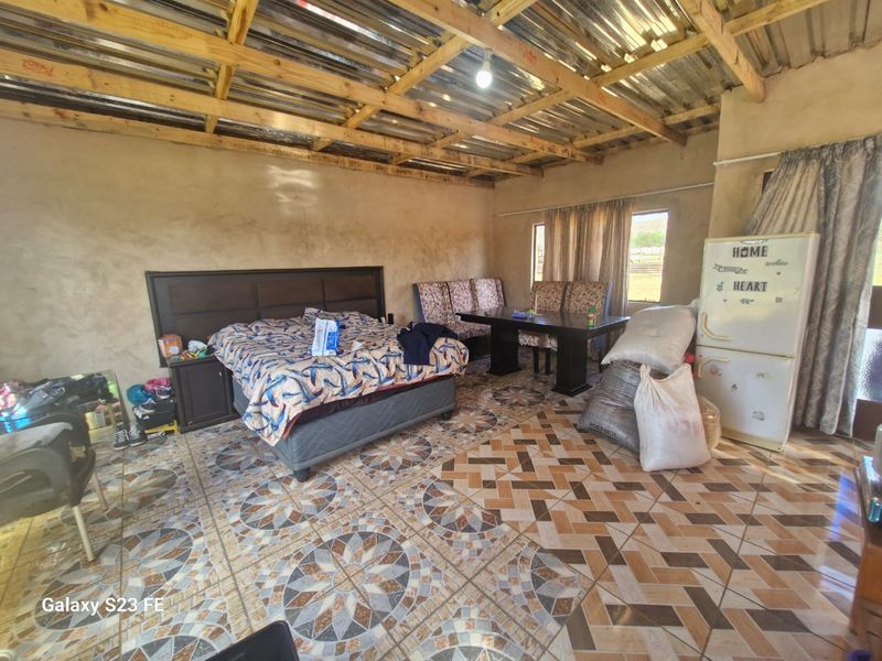 A bedroom featuring exposed timber roof trusses, corrugated metal ceiling, and patterned ceramic floor tiles with unfinished wall surfaces.