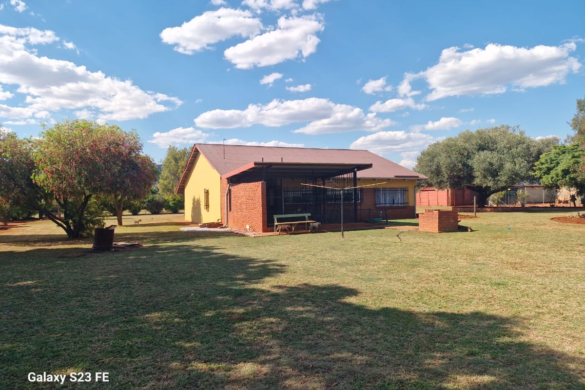 Rear view of a farm-style house featuring a covered patio, brick exterior walls, and a built-in brick braai area set within a spacious garden.