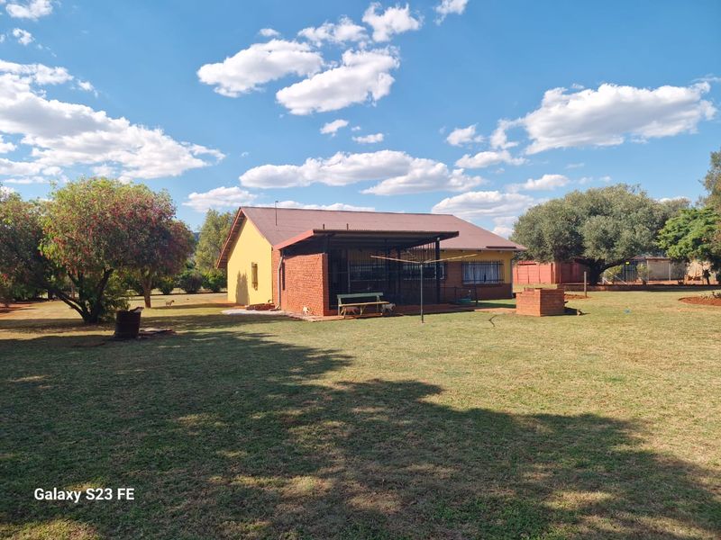 Rear view of a farm-style house featuring a covered patio, brick exterior walls, and a built-in brick braai area set within a spacious garden.