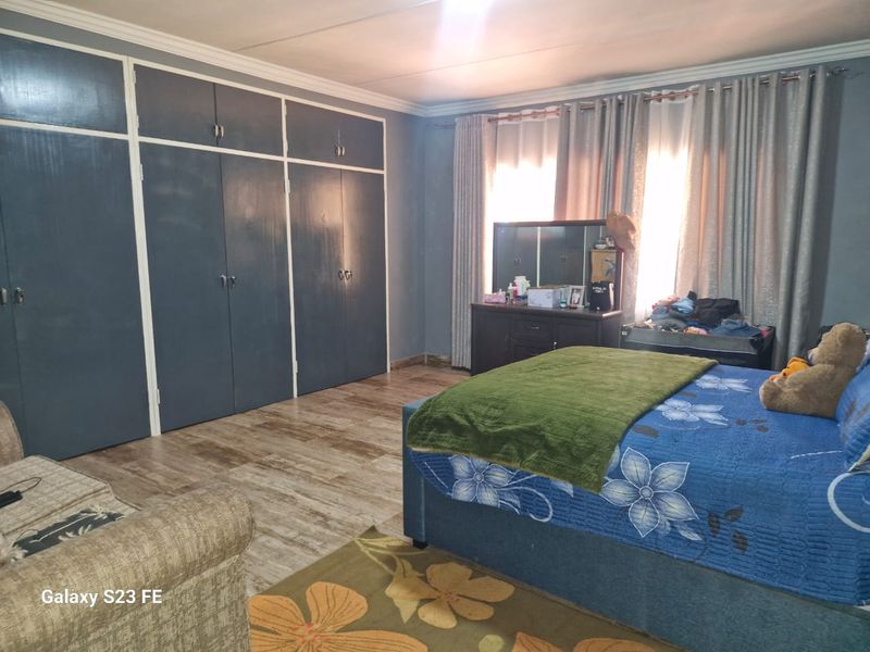Spacious bedroom featuring extensive built-in cupboards, modern laminate flooring, and decorative ceiling cornicing, offering a functional and comfortable living space.