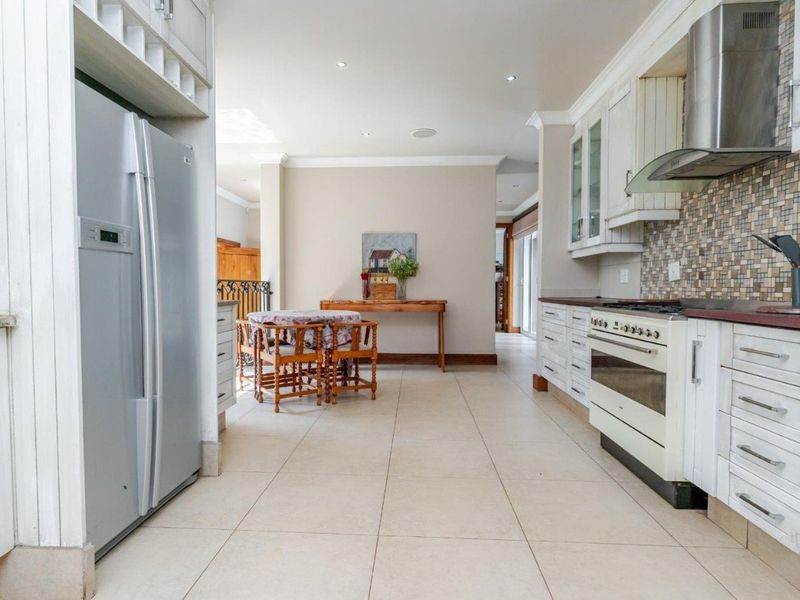 Spacious kitchen featuring white cabinetry, mosaic tile backsplash, gas stove with extractor fan, and neutral tiled flooring, flowing into an adjacent dining area.