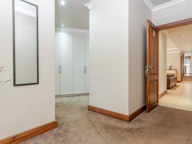 A clean, well-maintained hallway featuring neutral carpeting, built-in white cabinetry, and recessed lighting, providing access to adjacent living areas.