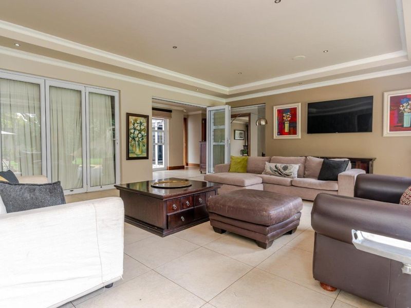 Spacious living room featuring tiled flooring, recessed ceiling lighting, crown molding, and large bi-fold glass doors providing access to the outdoor area.