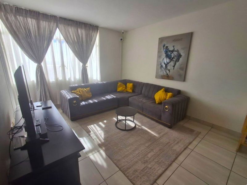 A comfortable living room featuring tiled flooring, neutral walls, and large windows with curtain treatments, providing a bright and functional space.