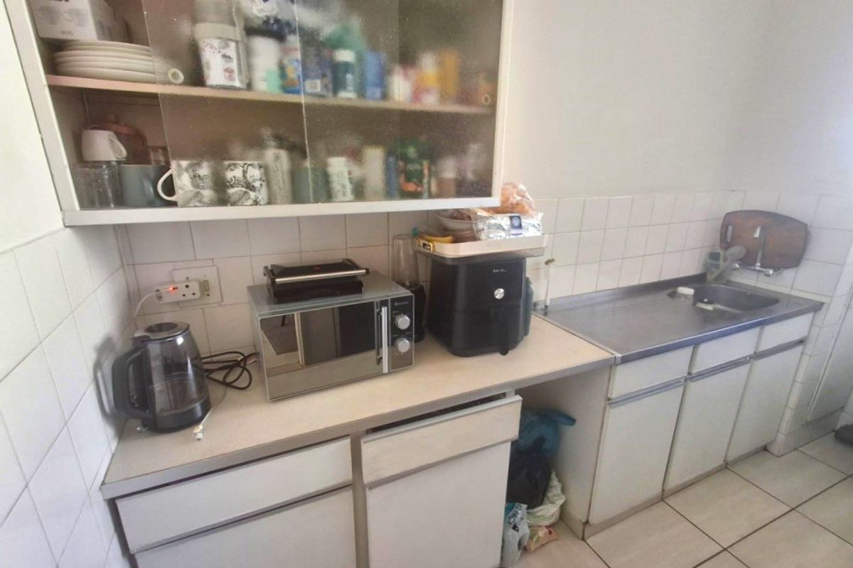 A compact kitchen featuring laminate countertops, a stainless steel sink, tiled backsplash, and original cabinetry, offering potential for a modern renovation.