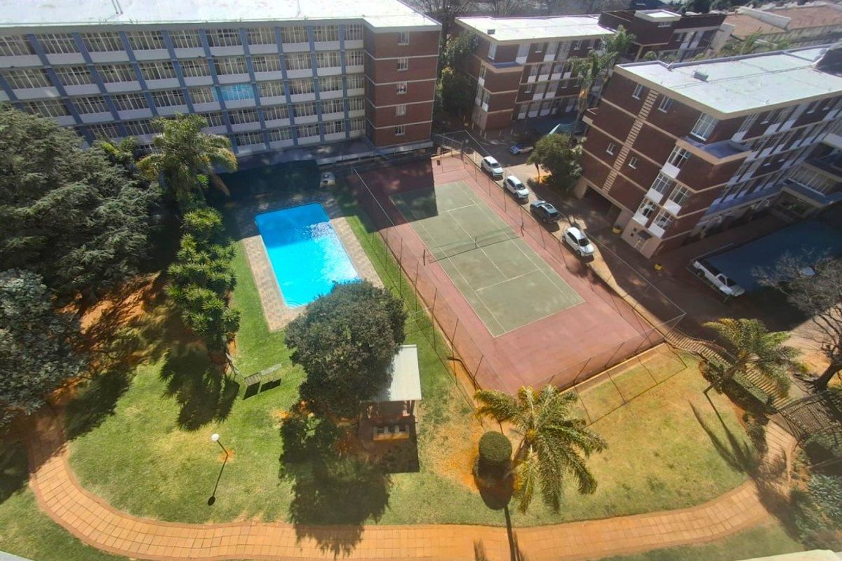 Aerial view of the apartment complex grounds featuring a swimming pool, tennis court, and well-maintained communal garden areas.