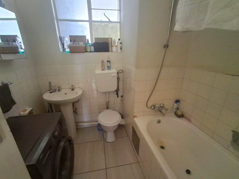 A functional bathroom featuring a pedestal basin, toilet, and bathtub with shower mixer, finished with tiled walls and flooring.