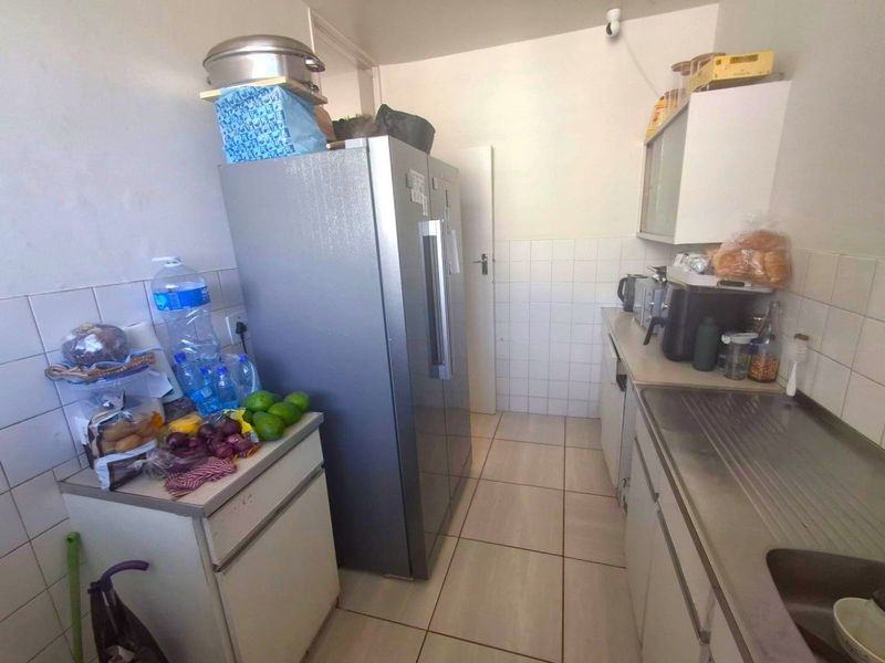 A compact kitchen featuring tiled splashbacks, built-in cabinetry, and a stainless steel sink, requiring cosmetic updates to improve its overall condition and appeal.