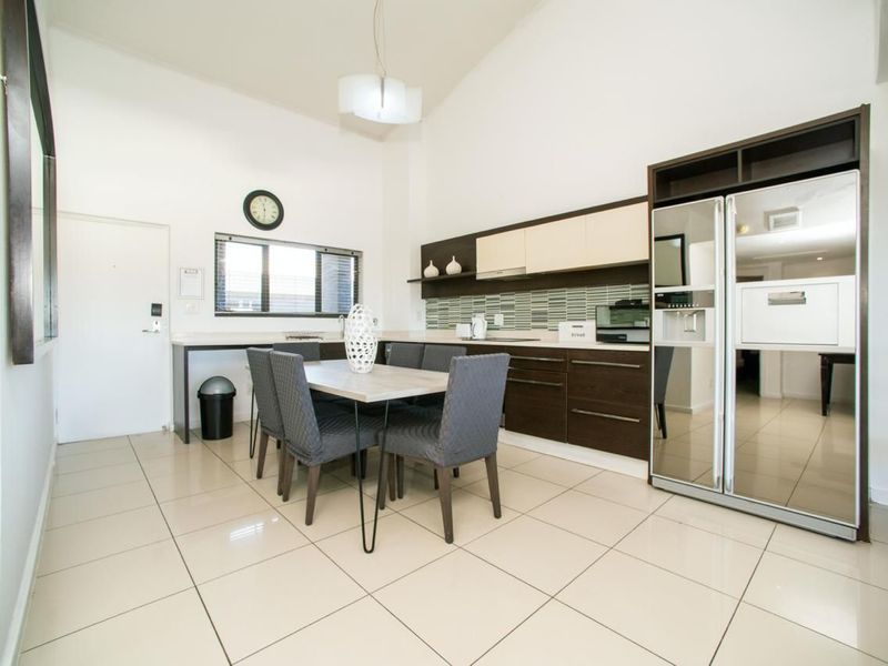 Modern open-plan kitchen and dining area featuring sleek dark cabinetry, tiled flooring, a tiled backsplash, and a high vaulted ceiling.
