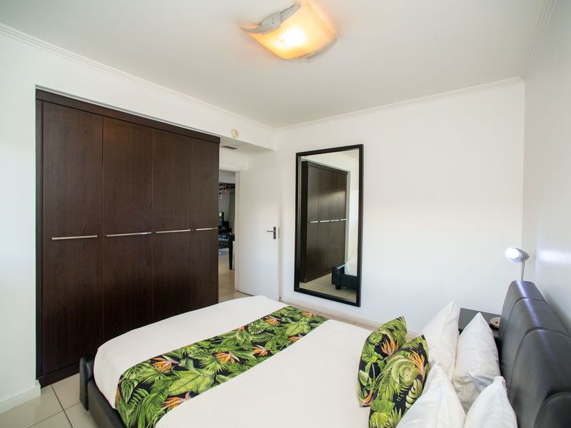 A well-maintained bedroom featuring dark wood built-in cupboards, tiled flooring, and a large wall-mounted mirror, providing a clean and functional living space.