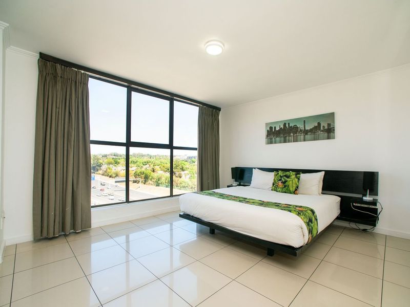 A bright and spacious bedroom featuring large floor-to-ceiling windows with expansive views, neutral tiled flooring, and a modern built-in headboard.