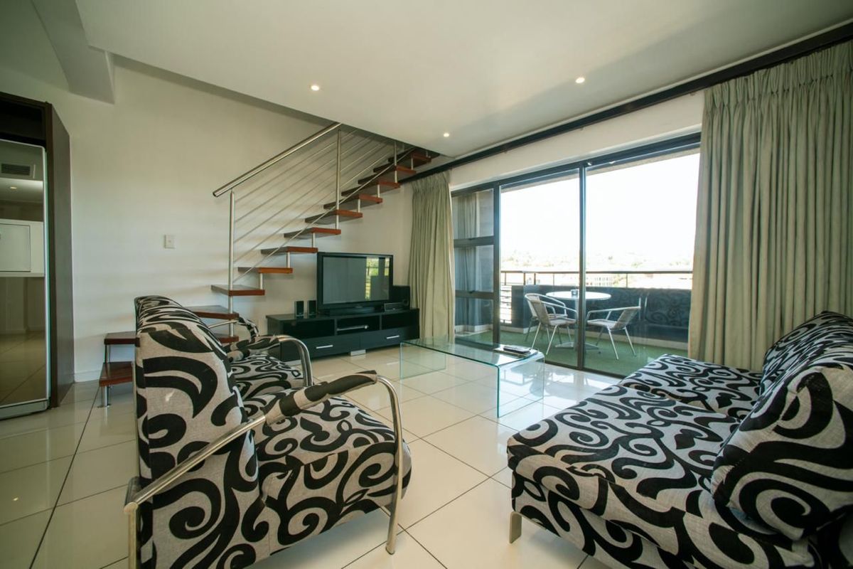 Open-plan living area featuring a modern staircase with stainless steel balustrade, large sliding glass doors leading to a balcony, and polished tiled flooring.