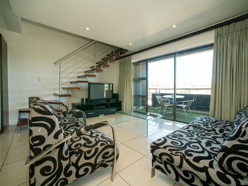 Open-plan living area featuring a modern staircase with stainless steel balustrade, large sliding glass doors leading to a balcony, and polished tiled flooring.