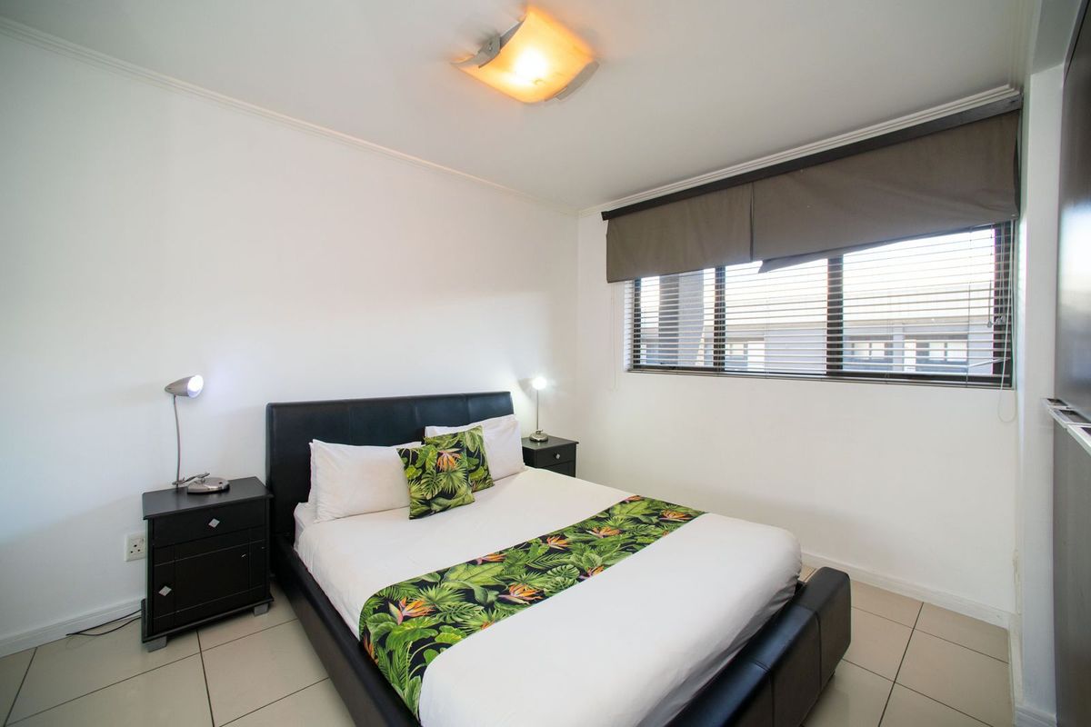 A well-maintained bedroom featuring tiled flooring, neutral walls, and window blinds, providing a clean and functional living space.