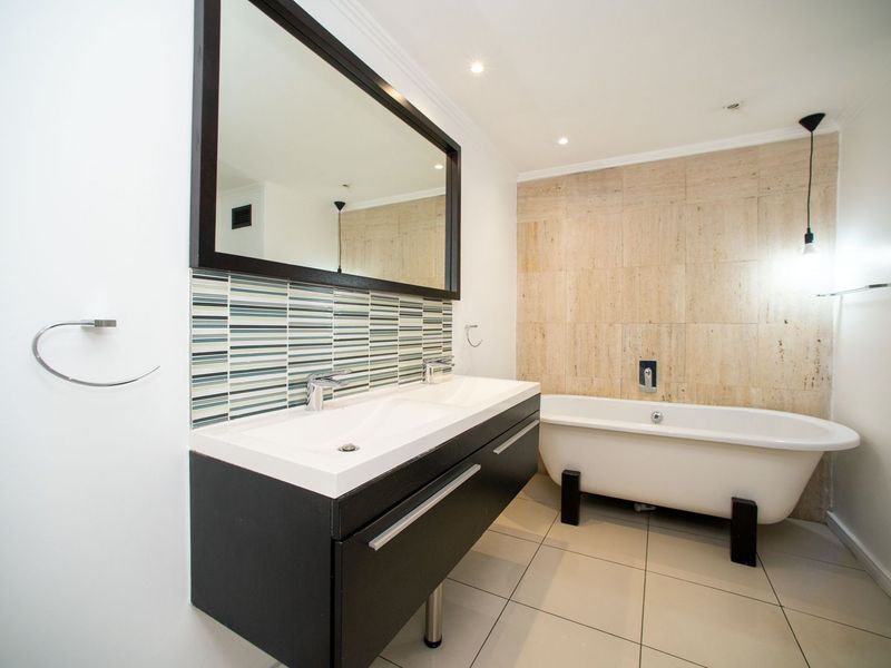 Modern bathroom featuring a double vanity with dark cabinetry, a freestanding bathtub, and elegant stone wall tiling.