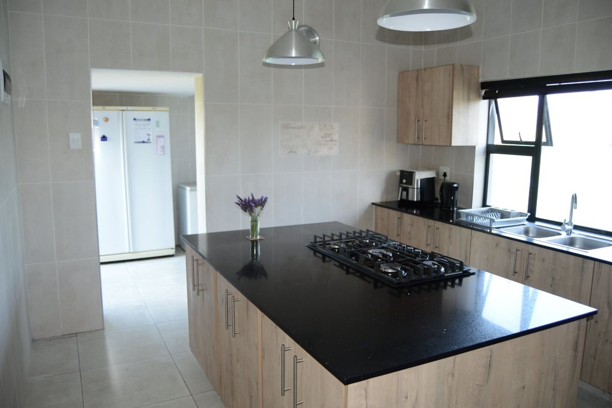 Modern kitchen featuring a central island with a gas hob, stone countertops, ample built-in cabinetry, and tiled finishes throughout.