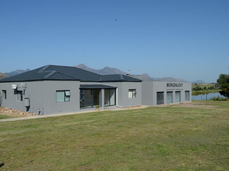 A well-maintained single-story farm building featuring a modern grey exterior, metal roofing, multiple garage bays, and sliding glass doors overlooking a scenic landscape.