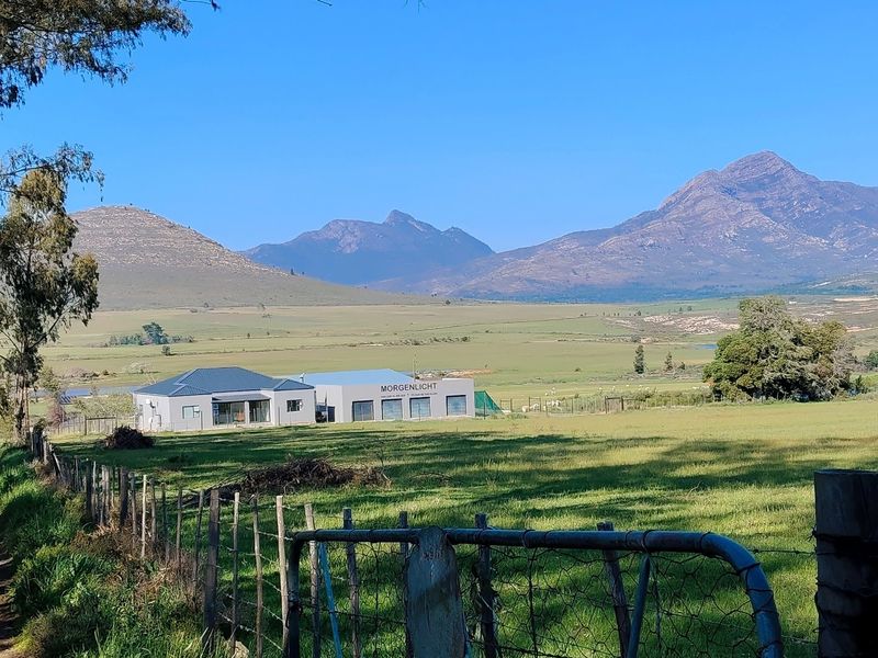 A scenic landscape view of the farm property featuring open pastures, mountain vistas, and the main farm buildings in the distance.