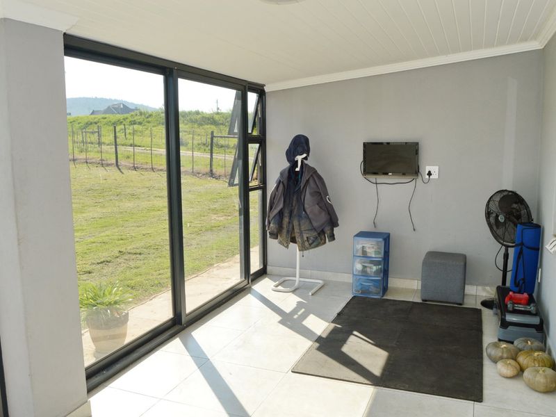 A bright, enclosed patio area featuring large sliding glass doors, tiled flooring, and a clean, neutral finish, offering views of the surrounding farm landscape.