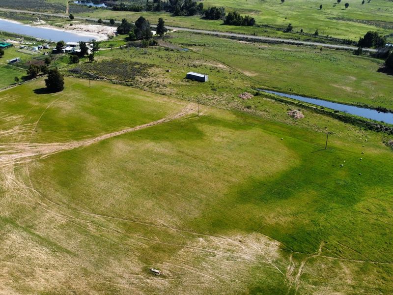 An aerial view of expansive farm land featuring open pastures, a natural waterway, and utility infrastructure.