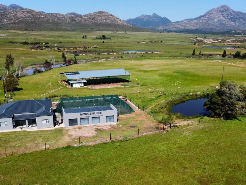 Aerial view of a farm property featuring a main residence, outbuildings, solar panels, and a scenic pond set against a mountain landscape.