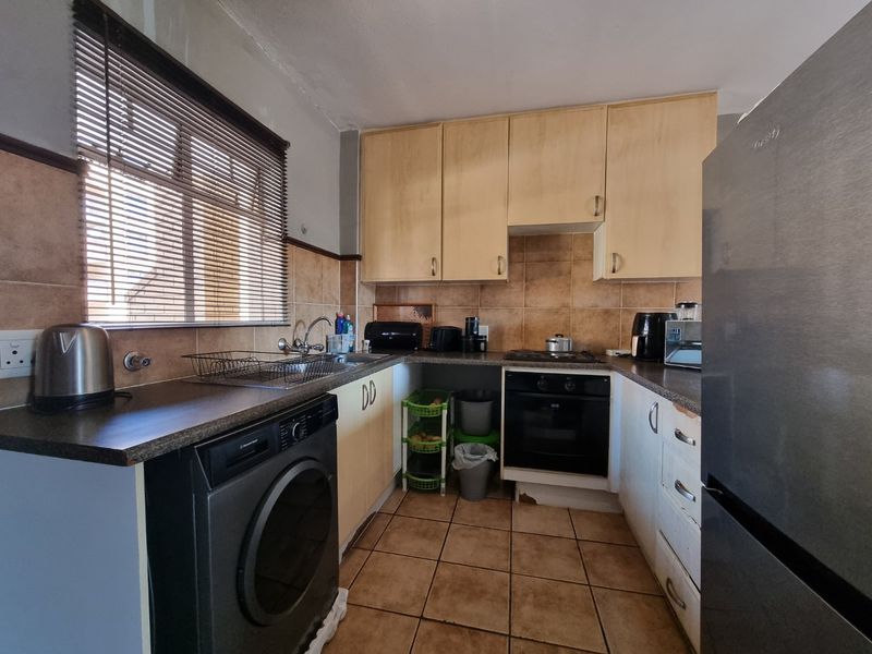 Compact kitchen featuring laminate cabinetry, tiled backsplash, built-in oven, and hob, with tiled flooring and a window with venetian blinds.