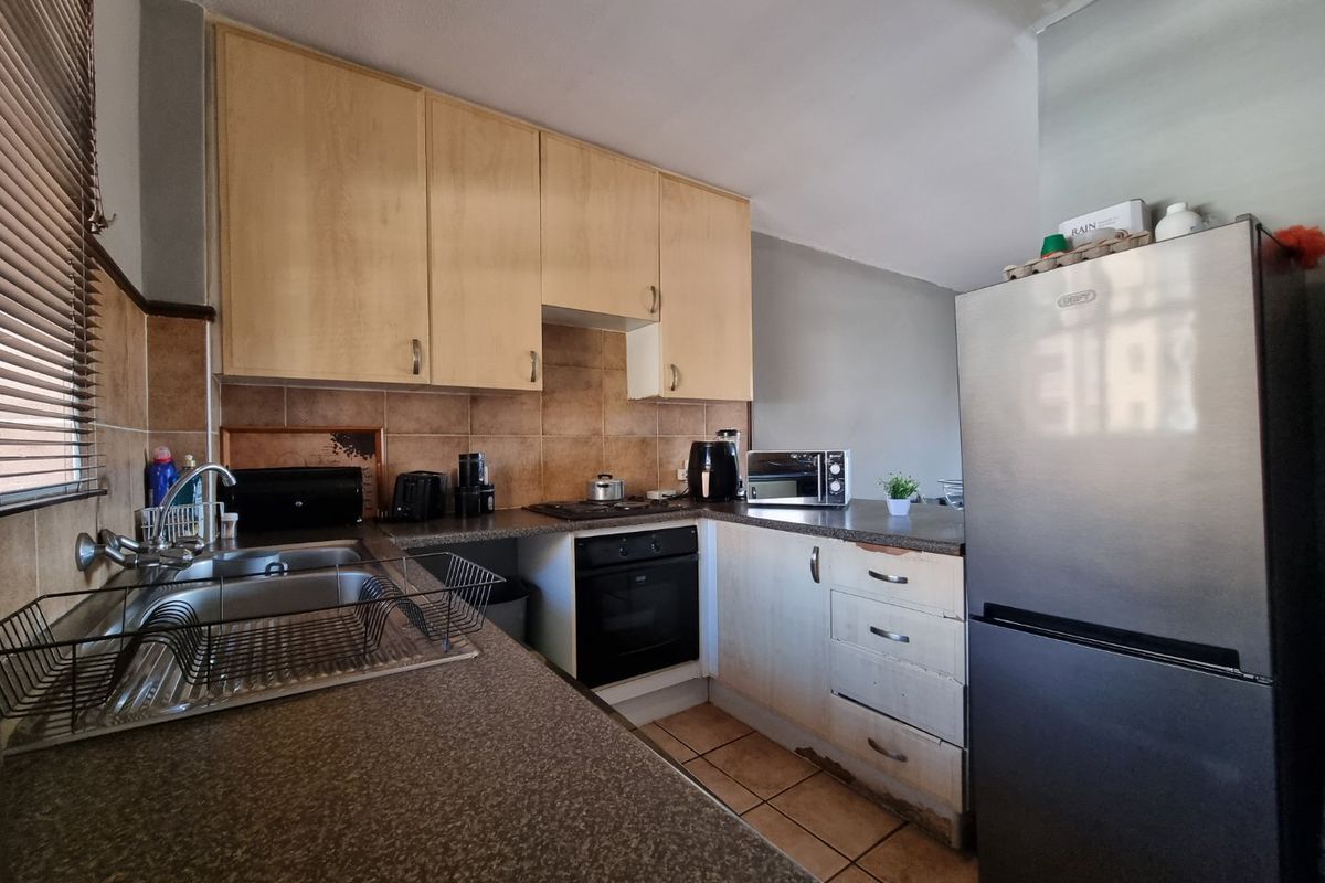 A functional kitchen featuring laminate cabinetry, built-in oven, hob, and tiled backsplash, showing signs of wear on the lower cabinet base.
