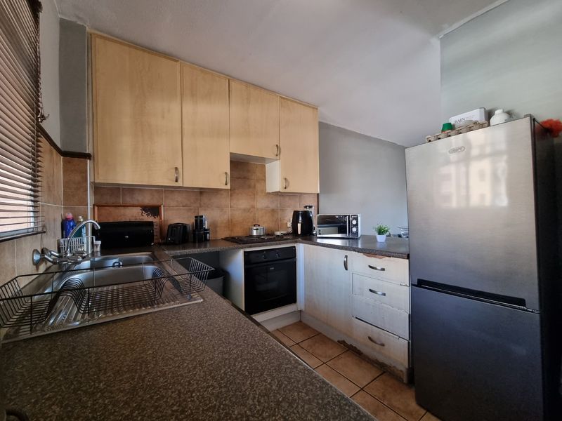 A functional kitchen featuring laminate cabinetry, built-in oven, hob, and tiled backsplash, showing signs of wear on the lower cabinet base.