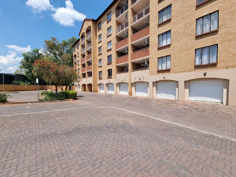 Exterior view of a multi-story apartment complex featuring brick facade, private balconies, and ground-level garage access with a paved driveway.