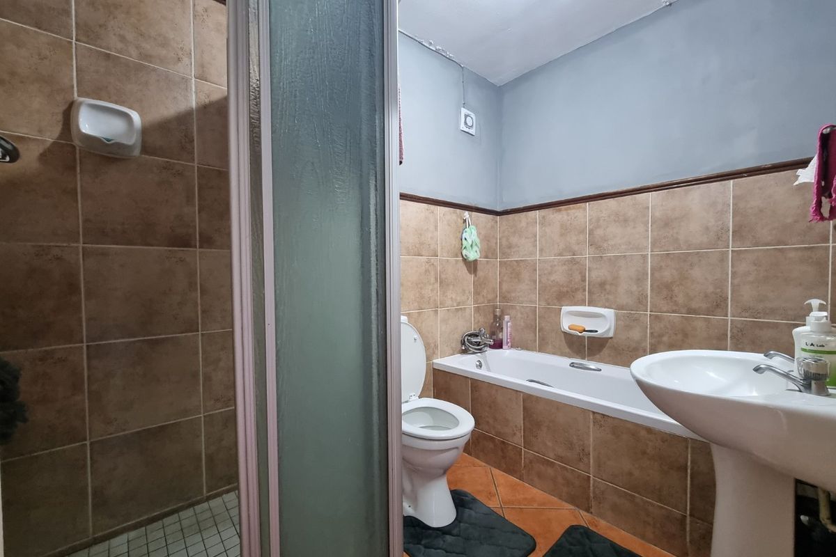 A functional bathroom featuring a separate shower enclosure, bathtub, pedestal sink, and toilet, with brown wall tiling and visible ceiling wear requiring maintenance.