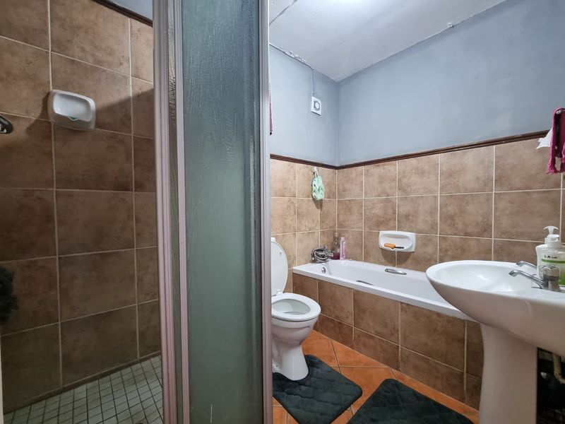 A functional bathroom featuring a separate shower enclosure, bathtub, pedestal sink, and toilet, with brown wall tiling and visible ceiling wear requiring maintenance.