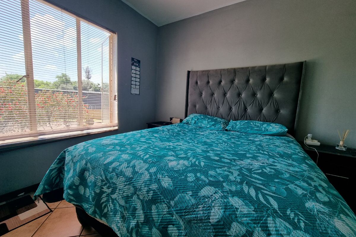 A well-lit bedroom featuring tiled flooring and a large window with venetian blinds, offering a comfortable and functional living space.
