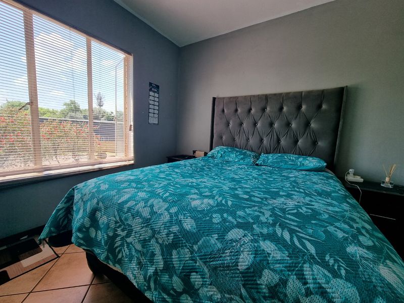 A well-lit bedroom featuring tiled flooring and a large window with venetian blinds, offering a comfortable and functional living space.