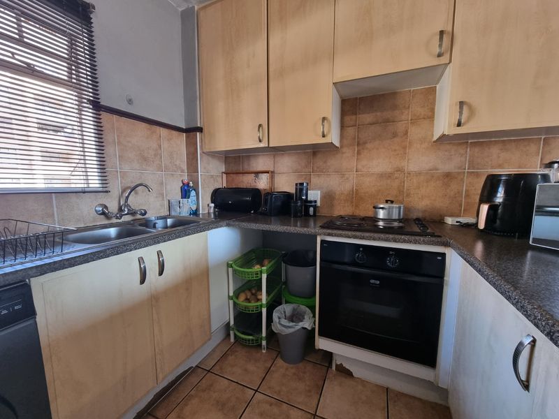 A compact kitchen featuring laminate cabinetry, tiled splashbacks, and built-in cooking appliances, showing signs of wear and dated finishes.