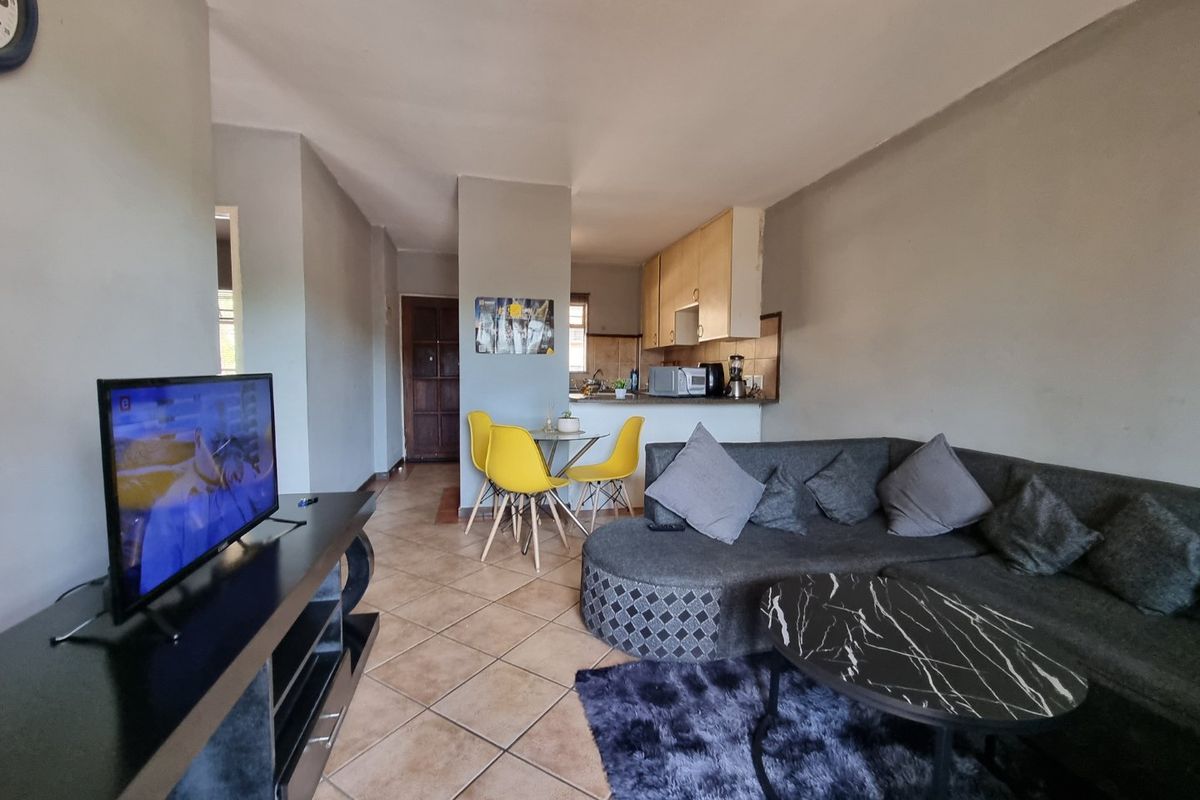Open plan living and dining area featuring tiled flooring and a compact kitchen with built-in cabinetry.