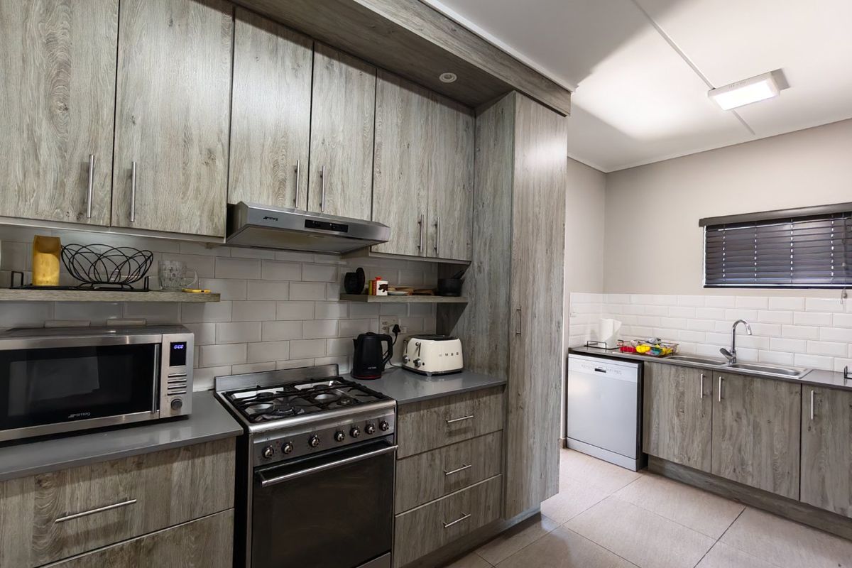 Modern kitchen featuring wood-look cabinetry, subway tile backsplash, gas hob, electric oven, and integrated stainless steel sink with tiled flooring.