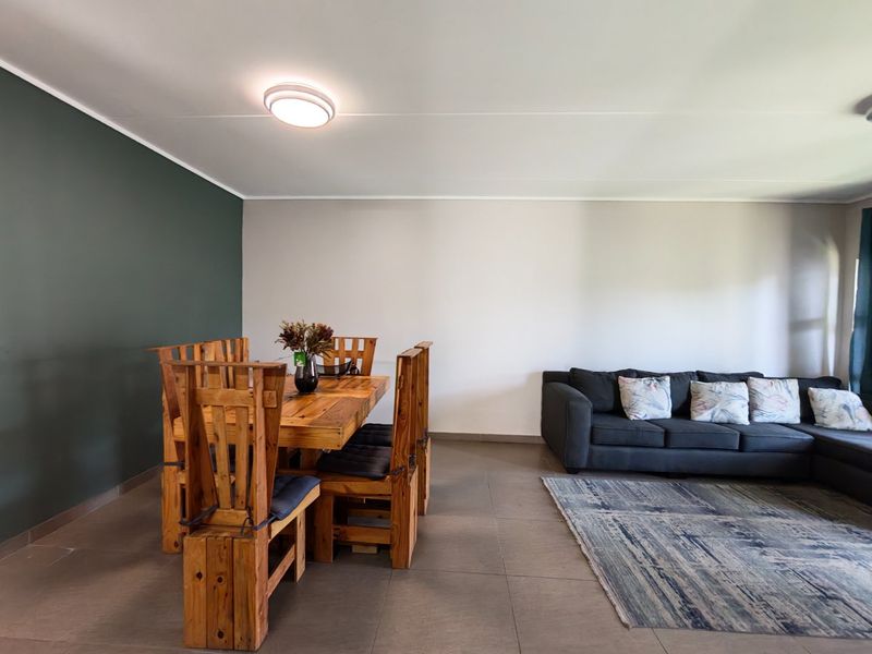 An open-plan living and dining area featuring neutral walls, a dark green accent wall, and large format floor tiles.