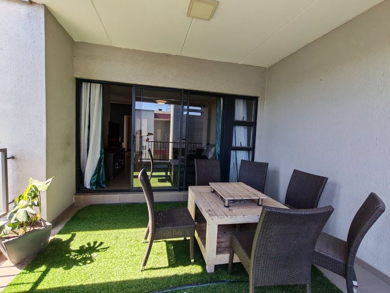 A covered balcony featuring artificial grass flooring and large sliding glass doors providing access to the interior living space.