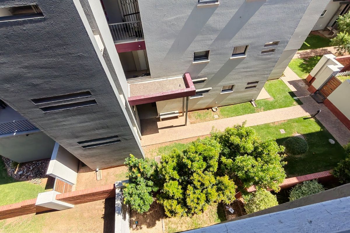 An elevated aerial view of an apartment complex exterior, featuring landscaped garden areas, paved walkways, and building facades with security features.