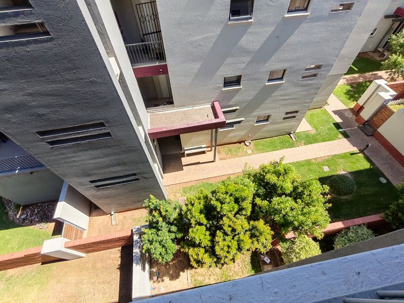 An elevated aerial view of an apartment complex exterior, featuring landscaped garden areas, paved walkways, and building facades with security features.