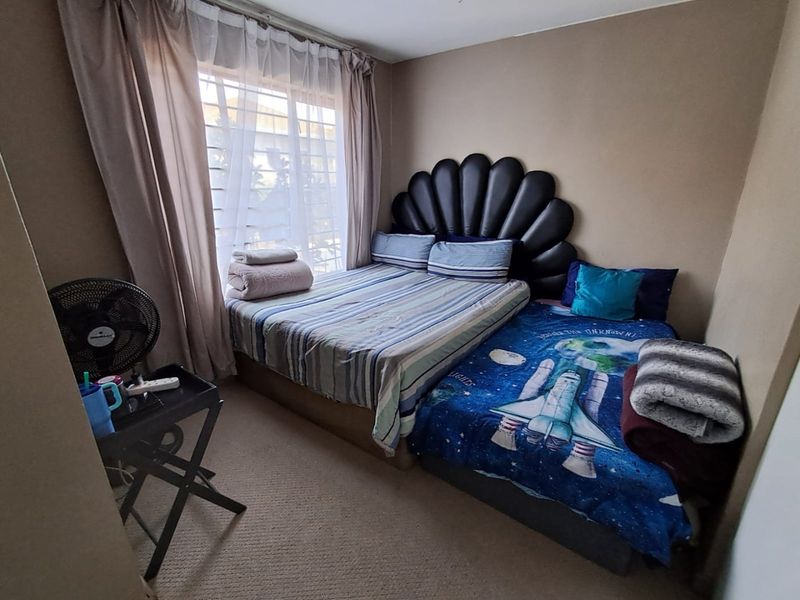 A compact bedroom featuring carpeted flooring and a large window fitted with security bars, providing natural light to the space.