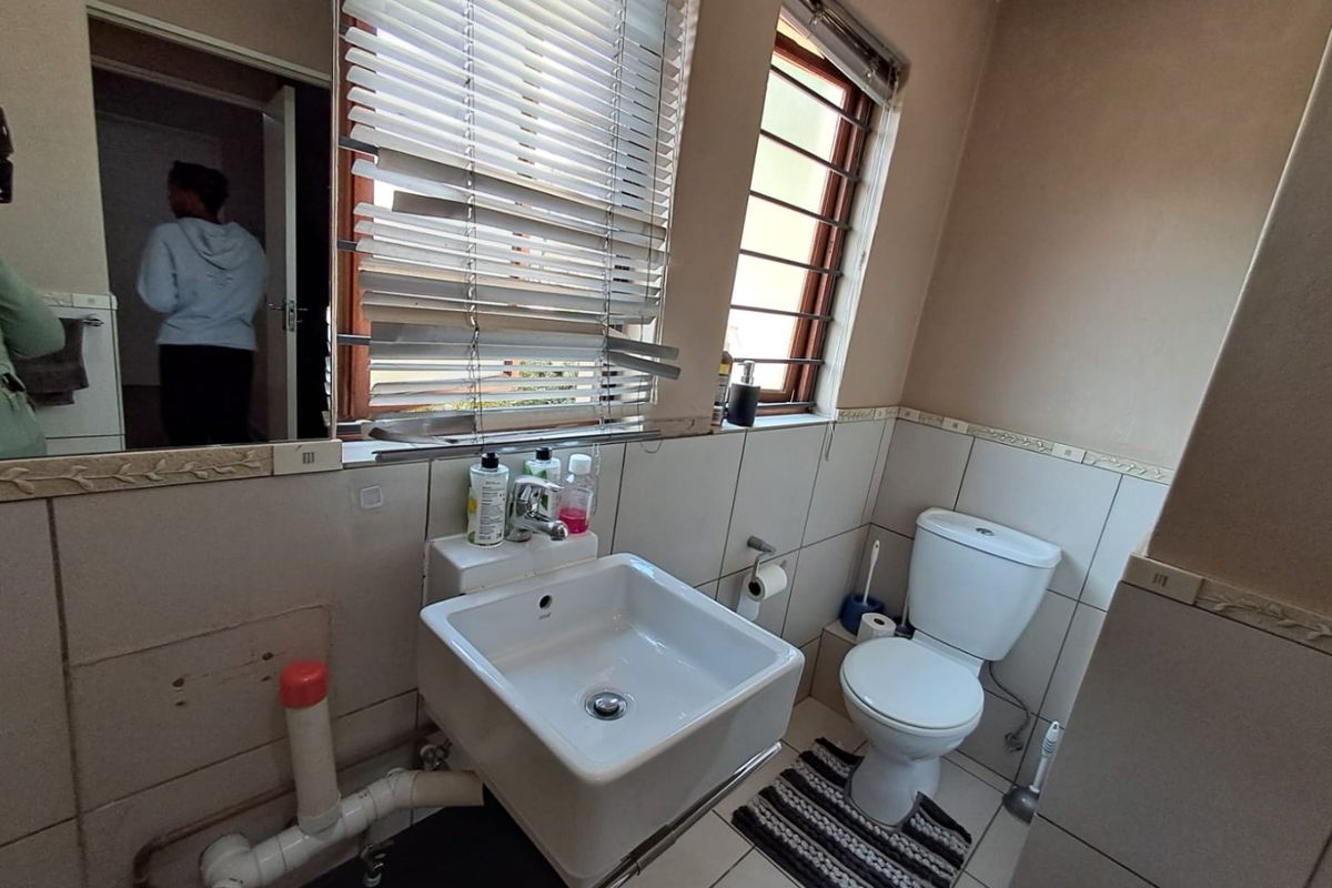 A compact bathroom featuring a wall-mounted basin, toilet, and tiled finishes. The space requires cosmetic updates and better concealment of exposed plumbing.